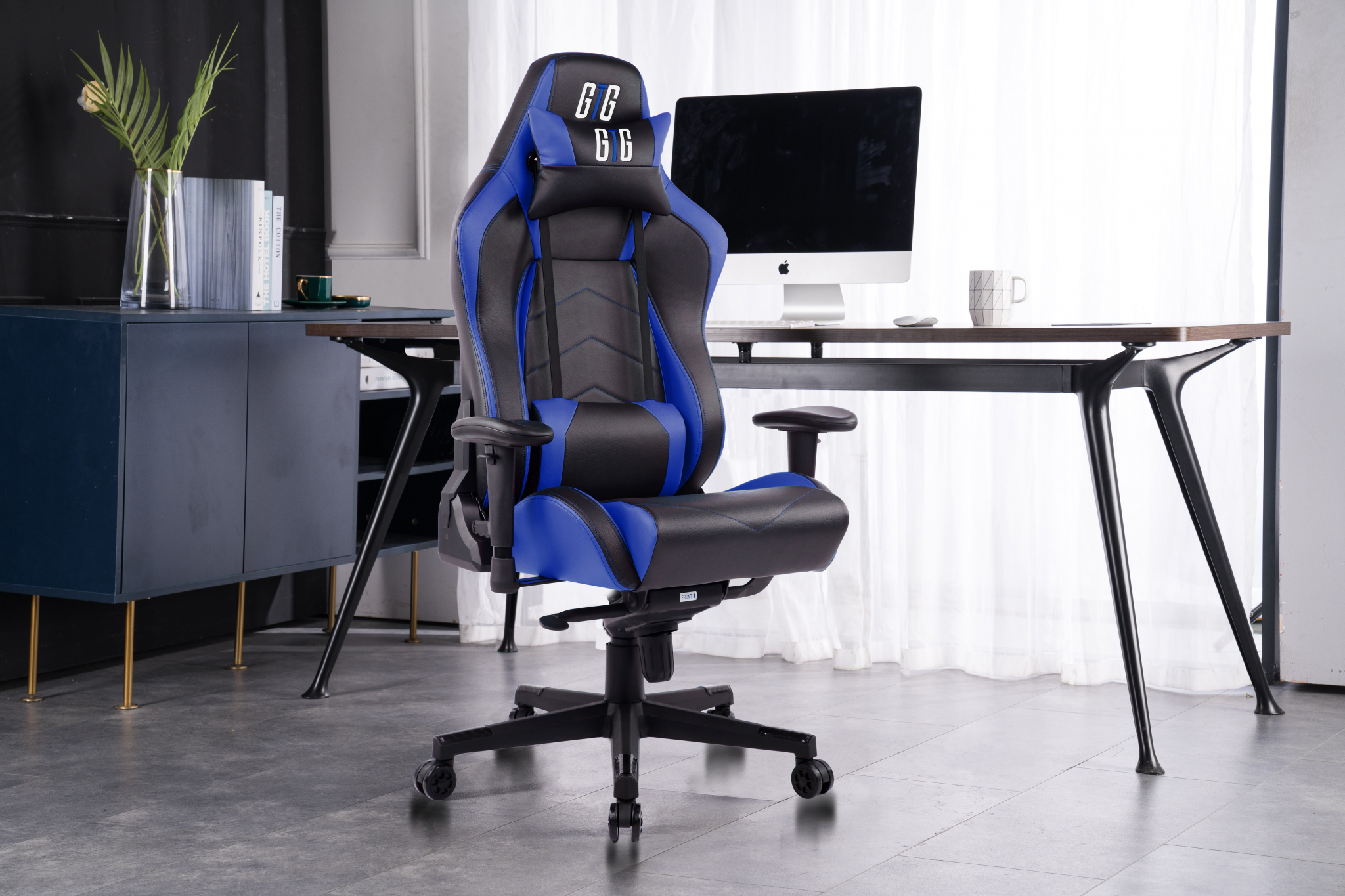 Ein blau-schwarzer Gaming-Stuhl. Ein Schreibtisch mit Computer und einigen Pflanzen ist im Hintergrund.