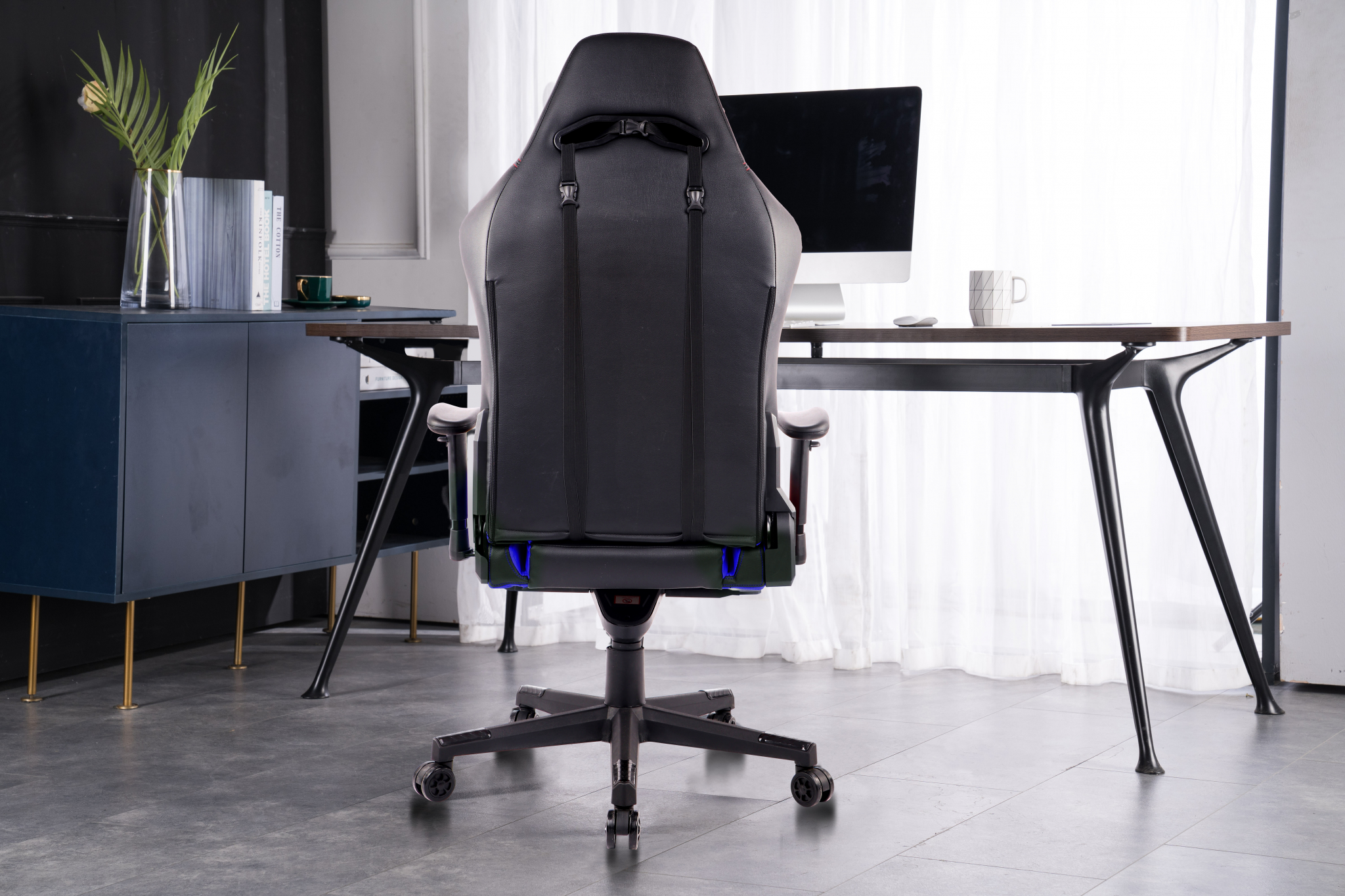 Rückansicht eines schwarzen Gaming-Stuhls mit Schreibtisch und Monitor im Hintergrund.