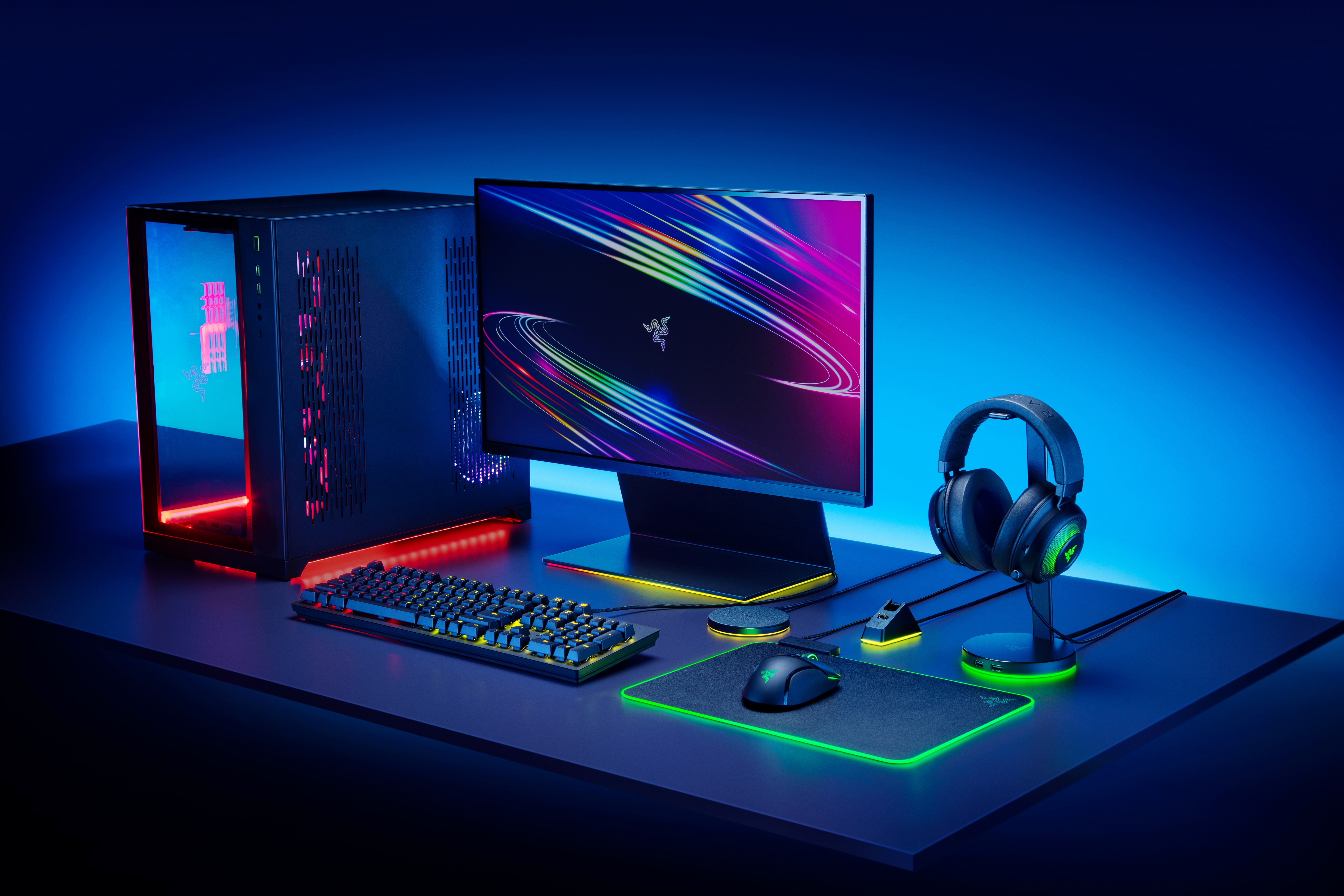 Gaming-Setup mit Monitor, Tastatur, Kopfhörern, Maus und Computerturm auf einem Schreibtisch, blaues Licht.