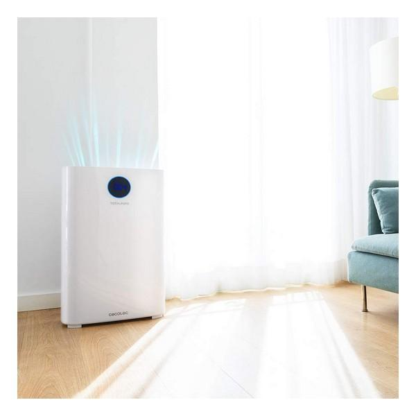 Purificatore d'aria bianco. È su un pavimento in legno. Finestra e divano sullo sfondo.