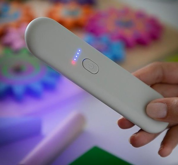 Graues UV-Handgerät mit Taste und Ladeanzeige, gehalten von einer Hand, auf weißer Oberfläche.