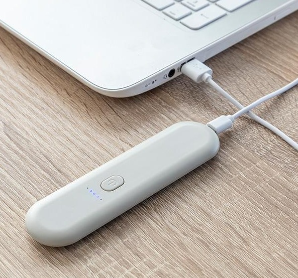 Ein weißes, tragbares Ladegerät, das mit einem weißen Kabel an einen Laptop angeschlossen ist.