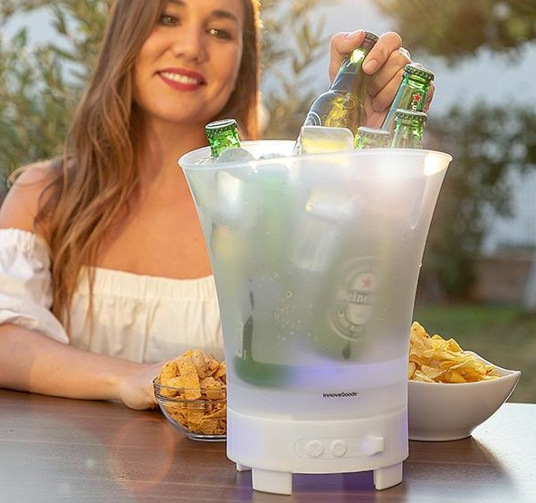 Eine Frau mit weißem Hemd hält einen beleuchteten Eisbehälter mit Bierflaschen und Snacks.
