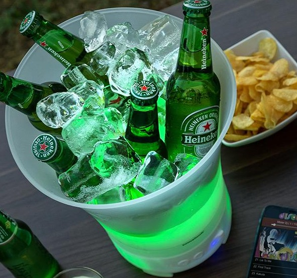 Bierflaschen in einem weiß-grünen Kühler mit Eis. Ein Smartphone und Chips sind sichtbar.