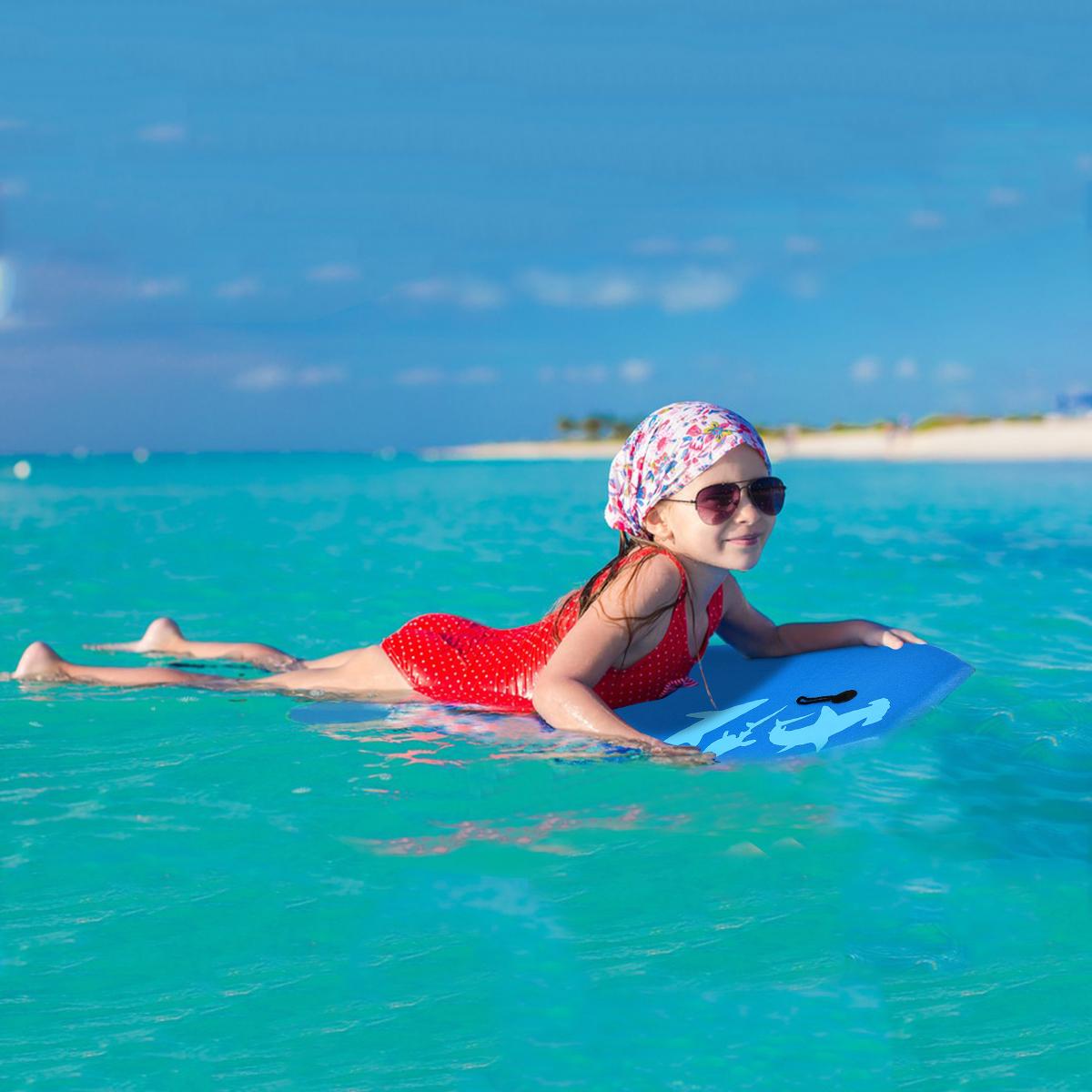Mädchen auf einem blauen Boogieboard in türkisfarbenem Wasser, trägt Badeanzug und Kopftuch.