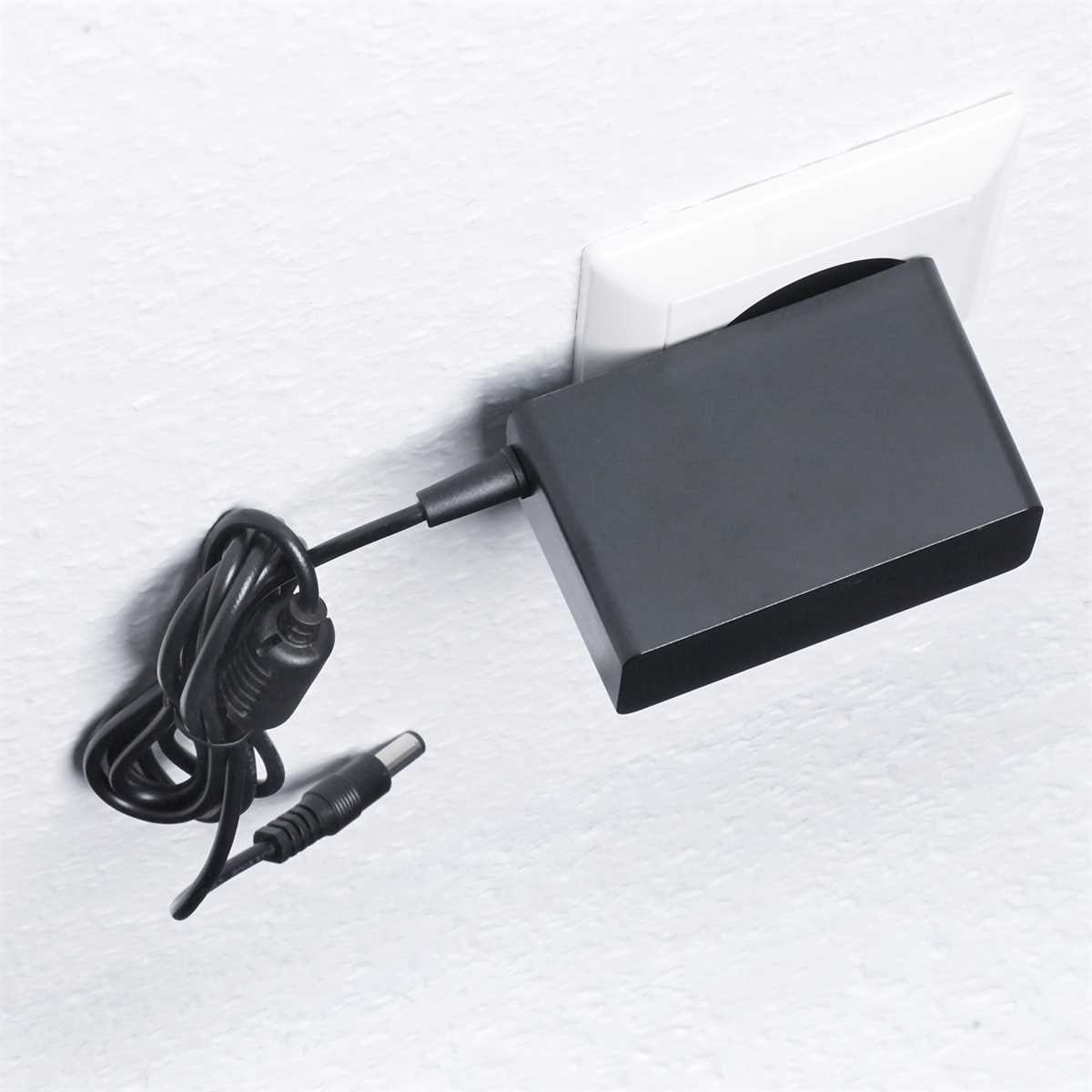 Schwarzes Ladegerät in einer weißen Steckdose an einer weißen Wand, mit losem Kabel.