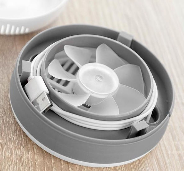 Ein kleiner grauer Ventilator mit weißen Flügeln und einem weißen USB-Kabel in einem grauen Gehäuse.