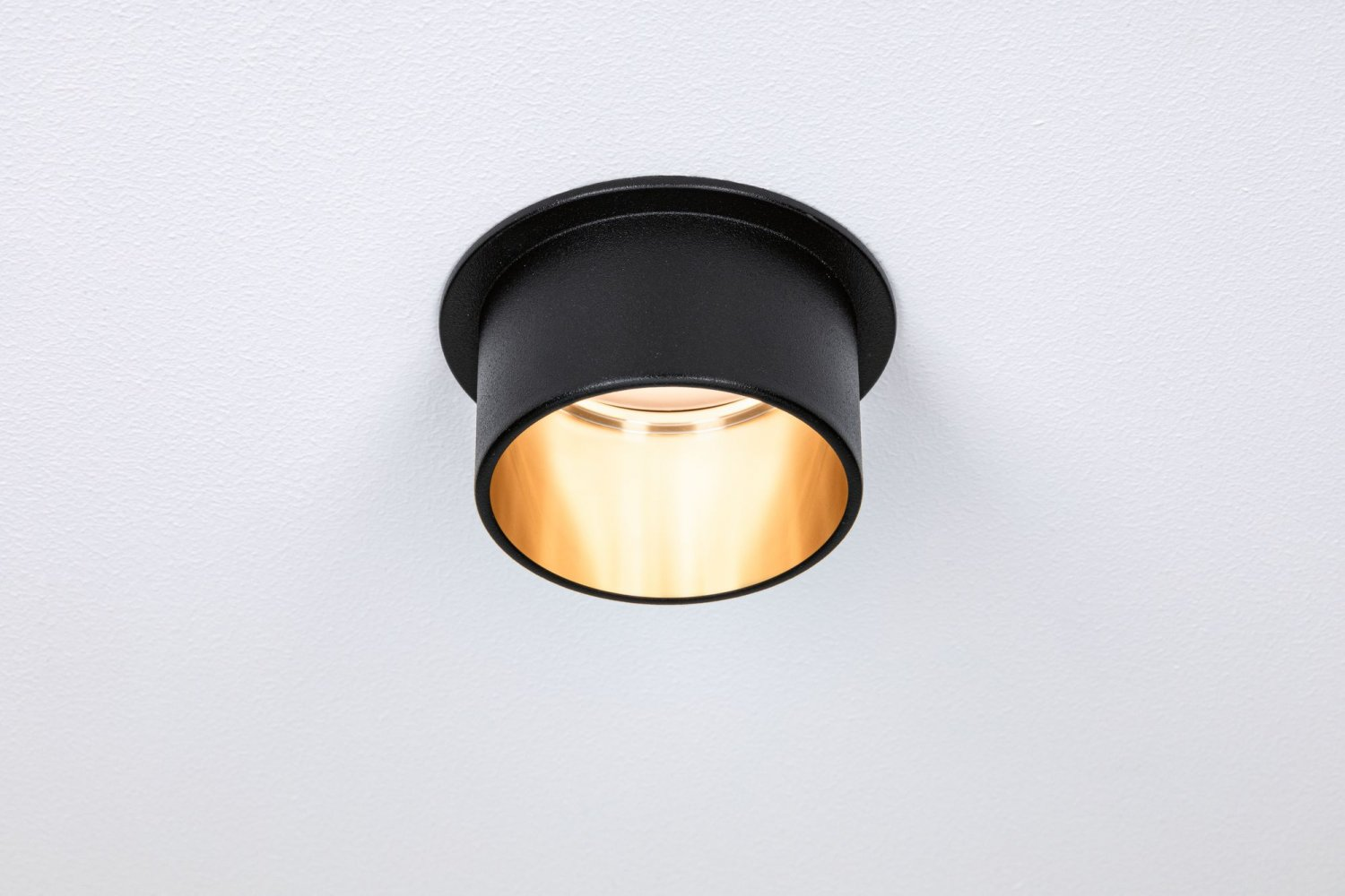 Eine schwarze Einbauleuchte mit goldenem Innenraum vor einer weißen Decke.