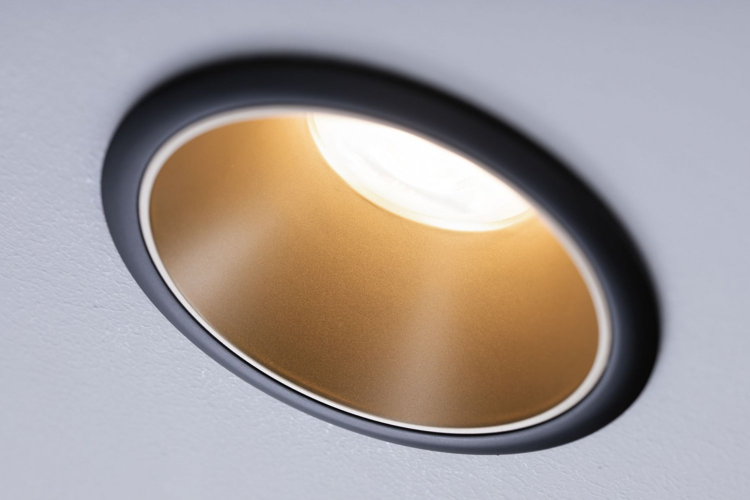 Apparecchio di illuminazione a incasso rotondo con bordo nero e interno dorato. Luce accesa.