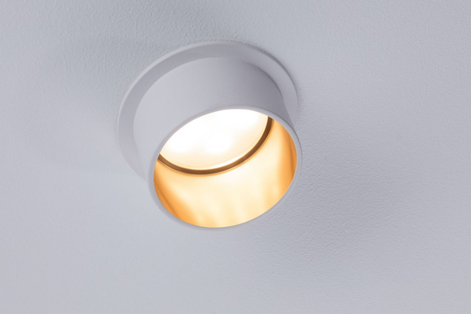 Ein einzelner Einbaustrahler, weißer Außenring, goldfarbener Innenraum, an einer weißen Decke.
