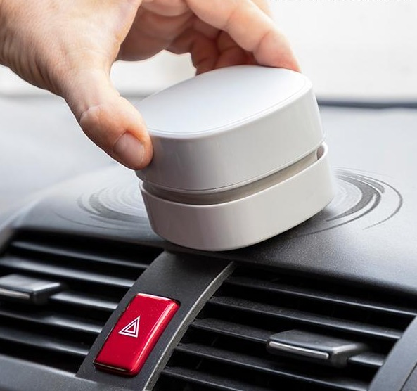 Una mano che usa un detergente bianco su un cruscotto dell'auto. Lo sfondo è un interno auto.