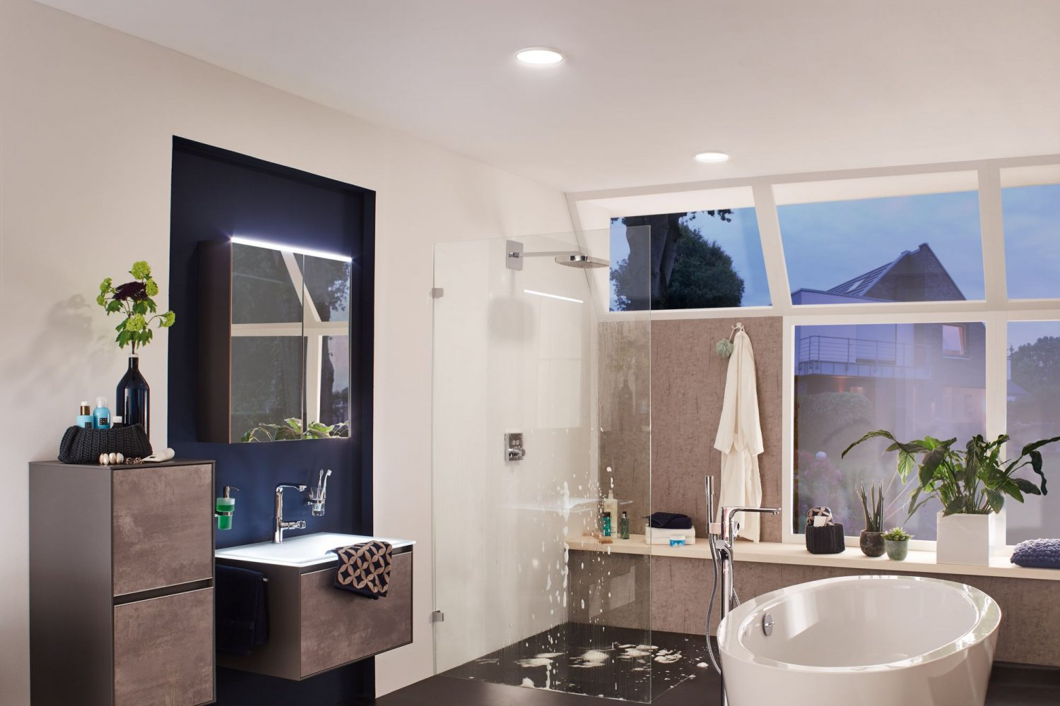 Modernes Badezimmer mit weißer Badewanne, Dusche und Waschtisch. Große Fenster und Spiegel sind vorhanden.