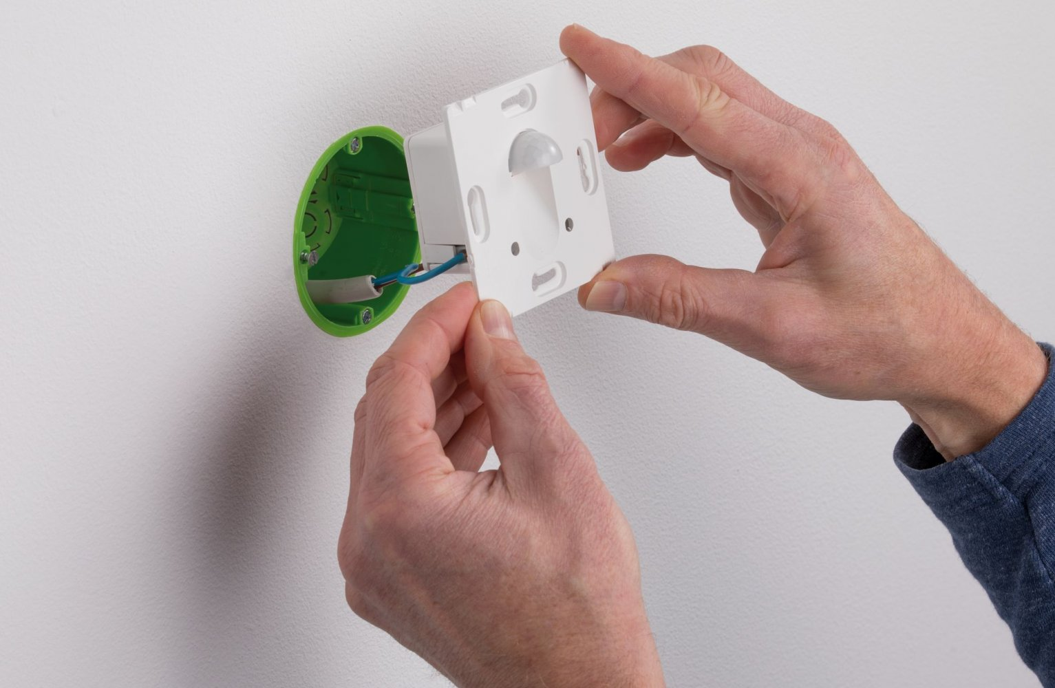 Eine Person installiert ein weißes quadratisches Gerät an einer Wand, mit einem grünen kreisförmigen Sockel.