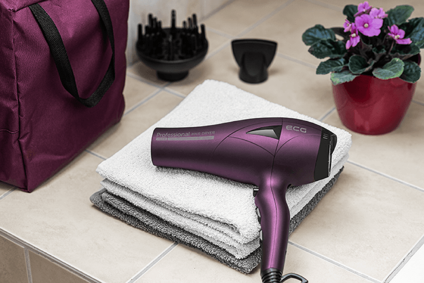 Fioletowa suszarka do włosów, ręczniki i akcesoria na kafelkowej powierzchni z rośliną.