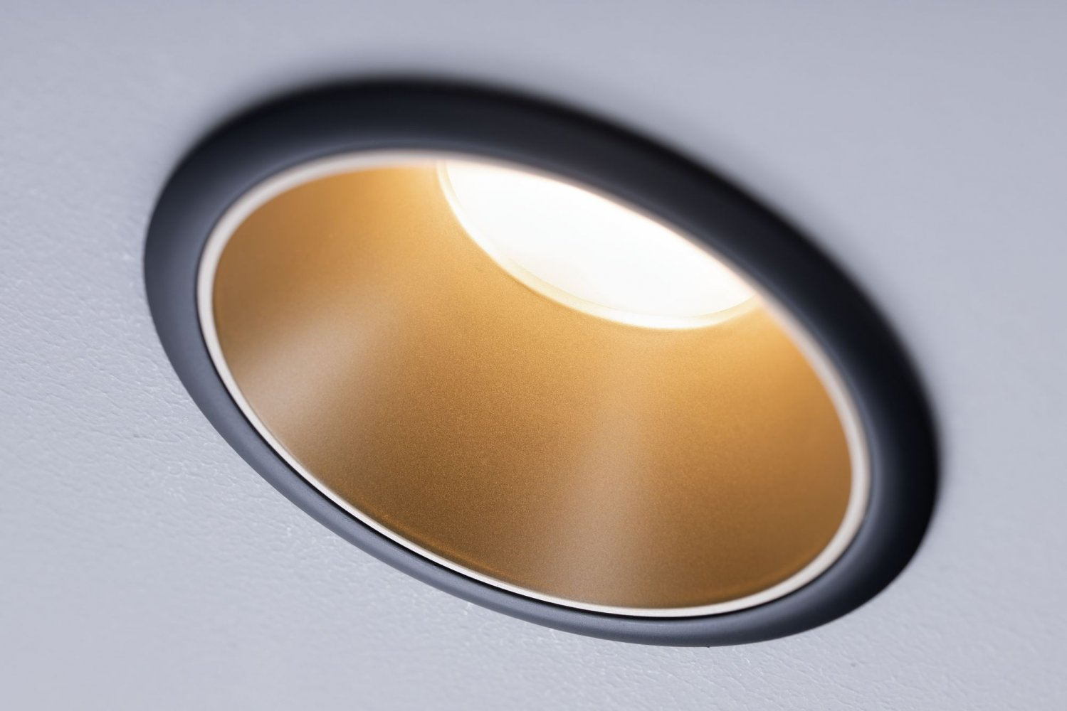 Nahaufnahme einer Einbauleuchte in einer weißen Decke. Das Licht ist an und strahlt einen warmen, goldenen Schein aus.