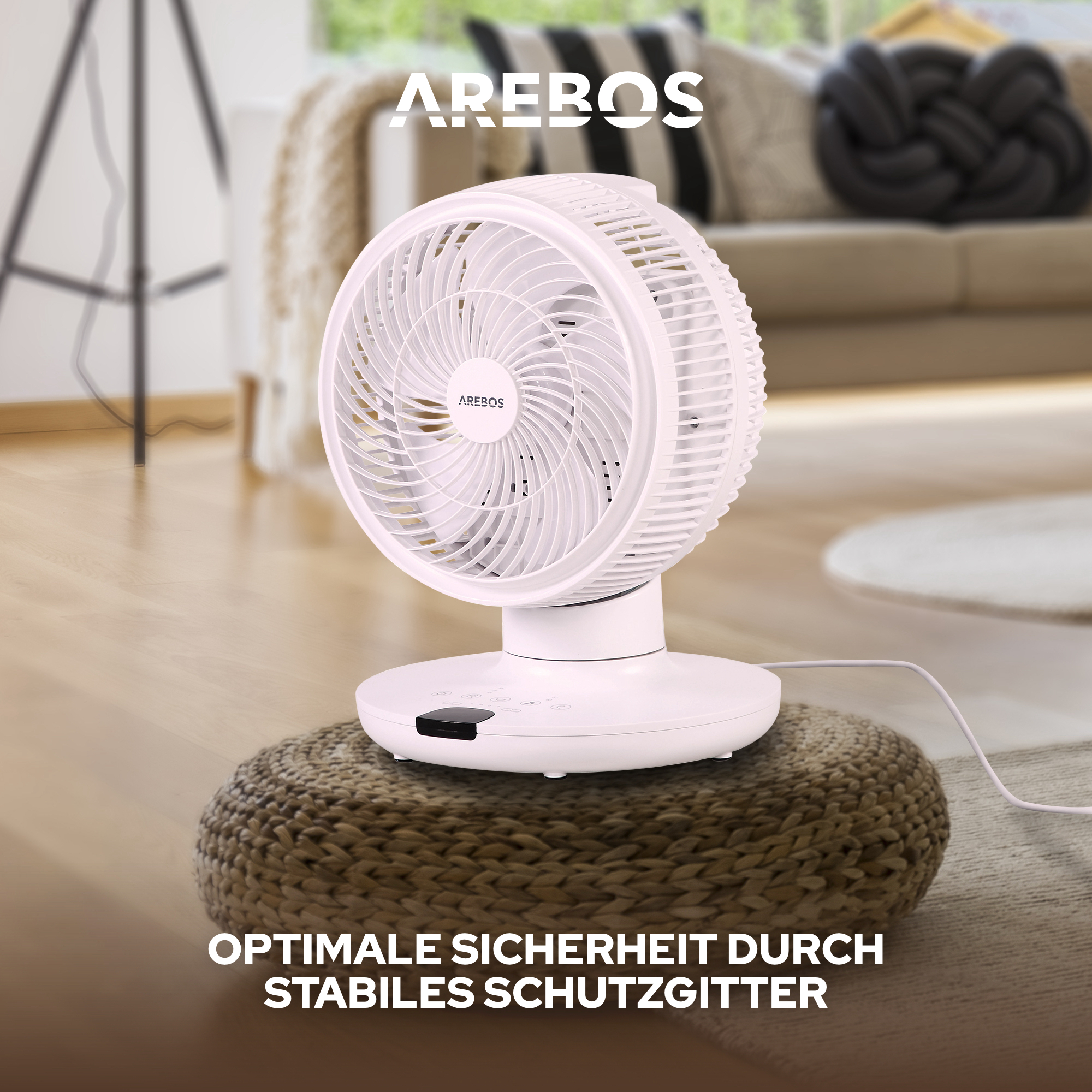 Ein weißer Ventilator auf einem gewebten braunen Kissen. Der Hintergrund umfasst eine Couch und einen dunklen geflochtenen Knoten.
