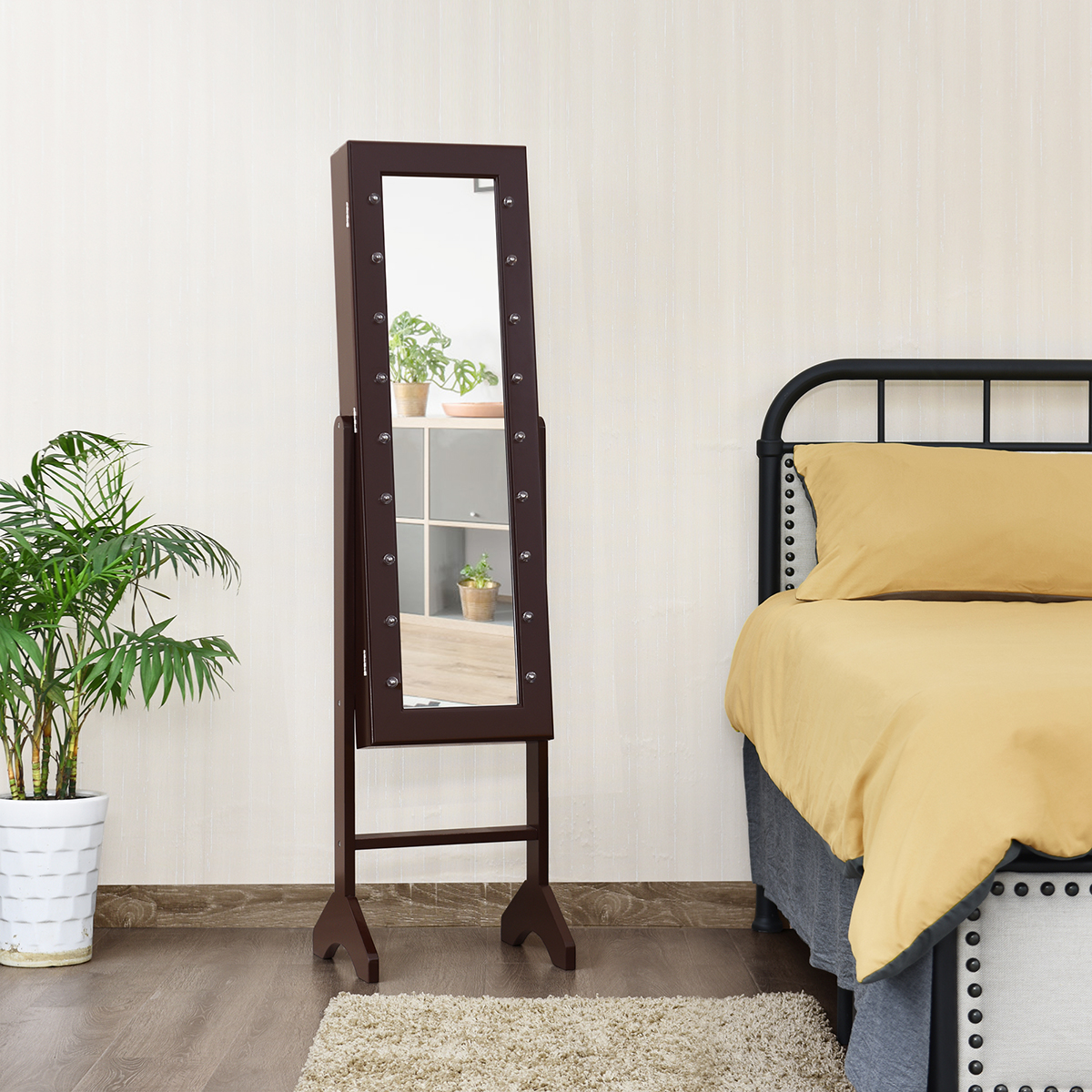 Hoher brauner Schmuckspiegelschrank mit Lichtern. Neben Bett und Pflanze.