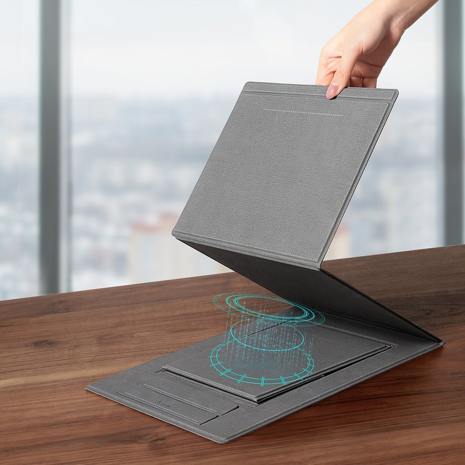 Ein grauer Laptop-Ständer, mit einer Hand, die ihn in Fensternähe öffnet.