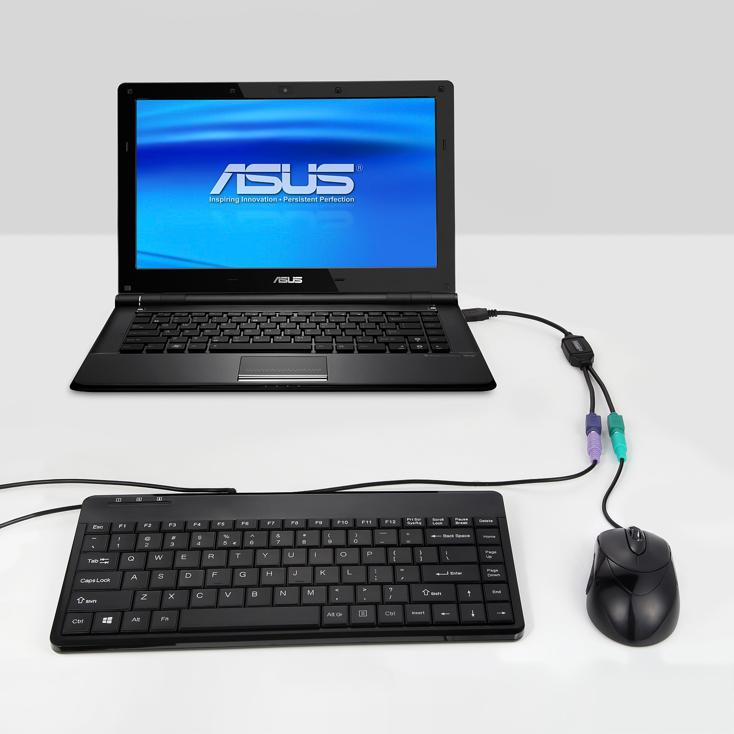 Ein Laptop, eine Tastatur und eine Maus, die mit Kabeln auf einem weißen Tisch verbunden sind.