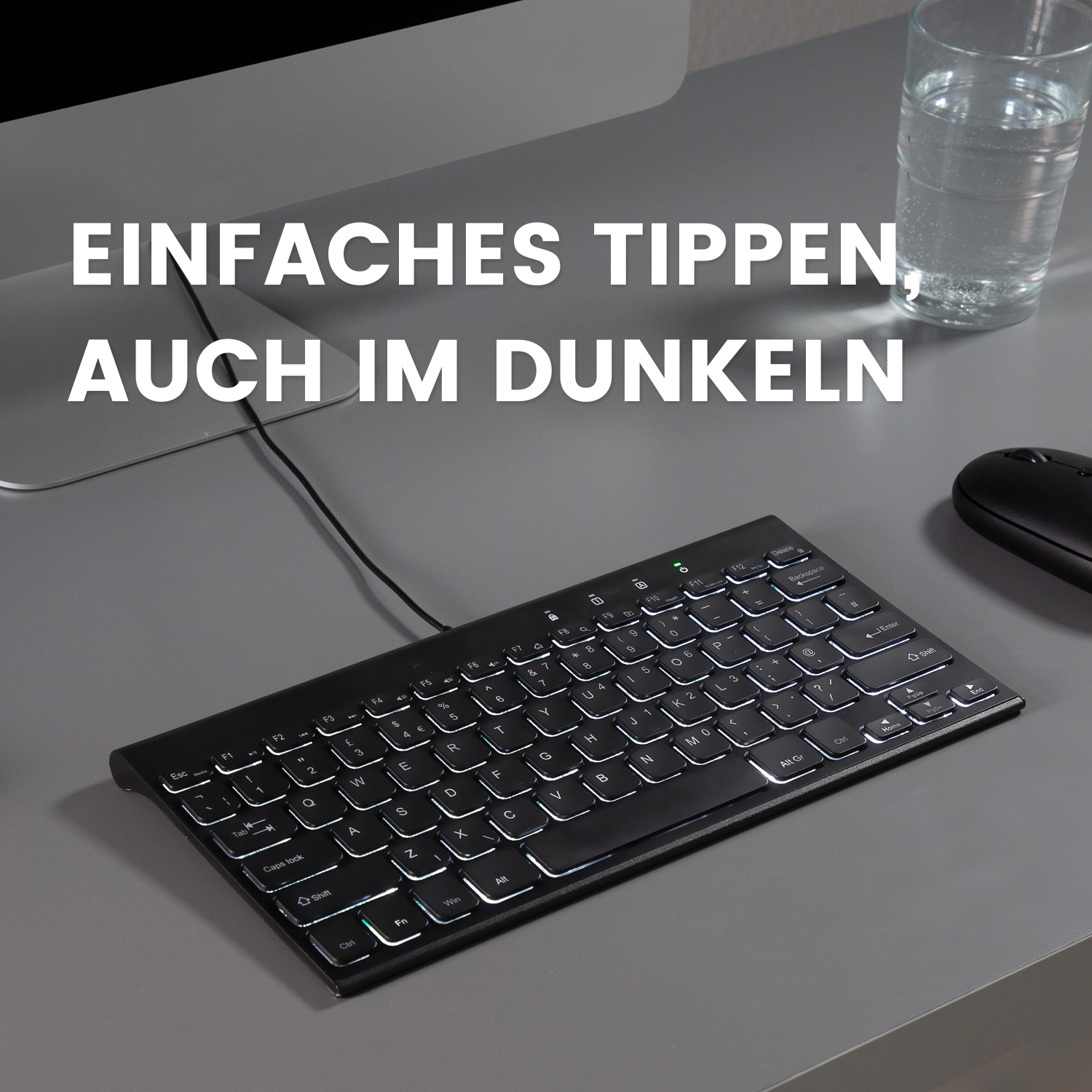 Schwarze Tastatur mit weißen beleuchteten Tasten auf einem grauen Schreibtisch mit Maus und Wasserglas.
