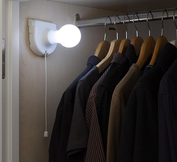Una lampadina bianca, su un'apparecchiatura bianca, all'interno di un armadio scuro con vestiti.