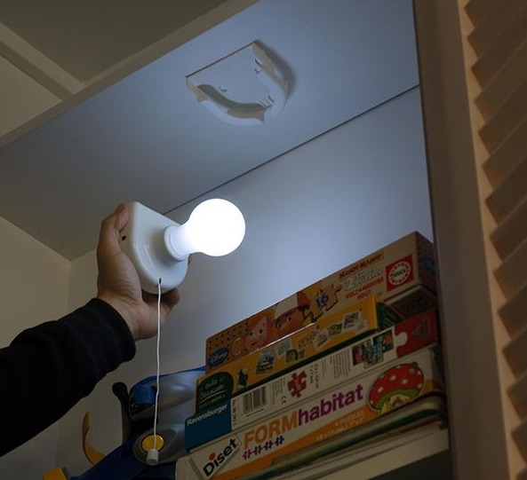 Una mano tiene una lampadina dal soffitto. Scaffali con giocattoli sullo sfondo.