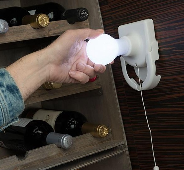 Una mano che tiene una lampadina vicino a bottiglie di vino in una rastrelliera. C'è una lampada a corda.