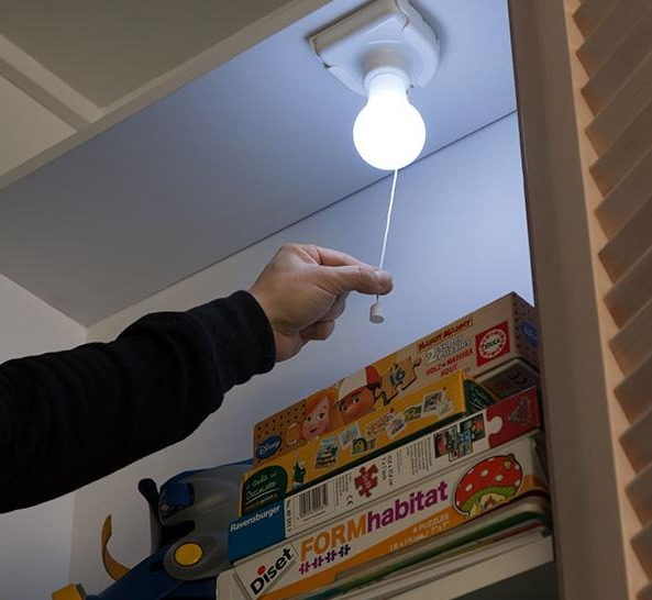 Mano che tira un filo della lampadina dentro un armadio con scatole impilate.