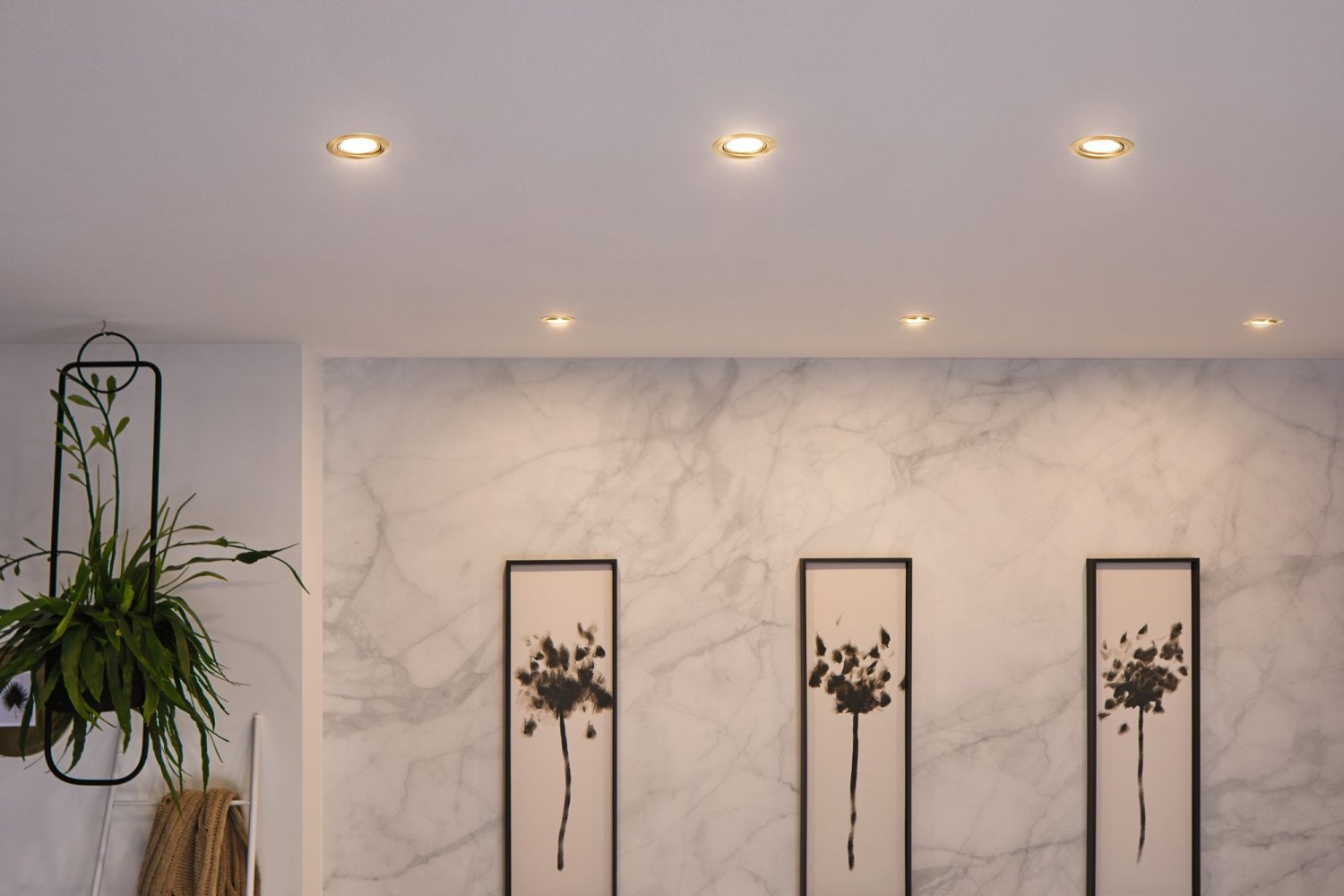 Faretti a soffitto. Tre quadri con disegni floreali neri su muro di marmo.
