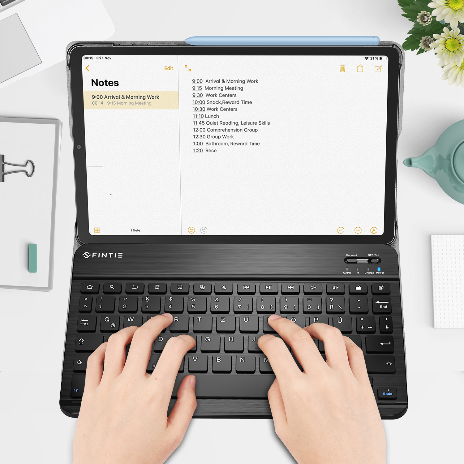 Hände, die auf einer schwarzen Tastatur tippen, die mit einem Tablet mit Zeitplan verbunden ist. Ein Stift liegt oben.