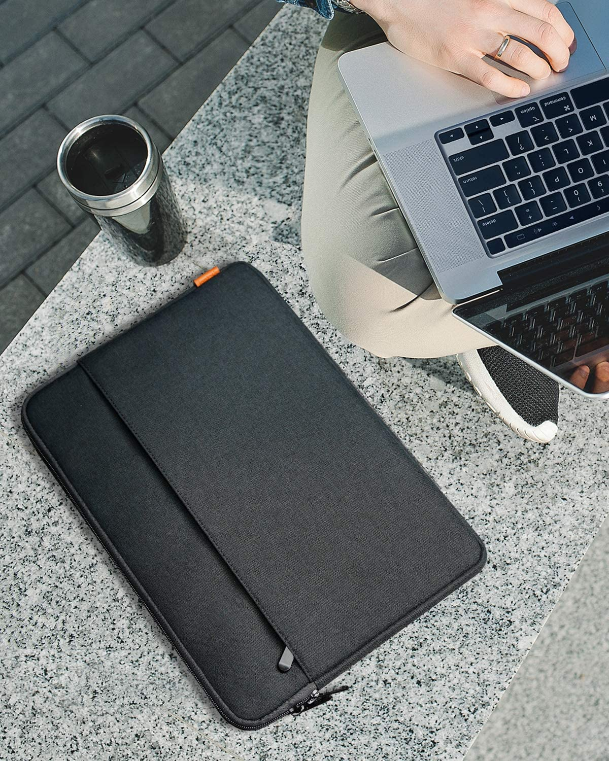 Person mit Laptop, schwarzer Hülle und einer Tasse auf einer Oberfläche.