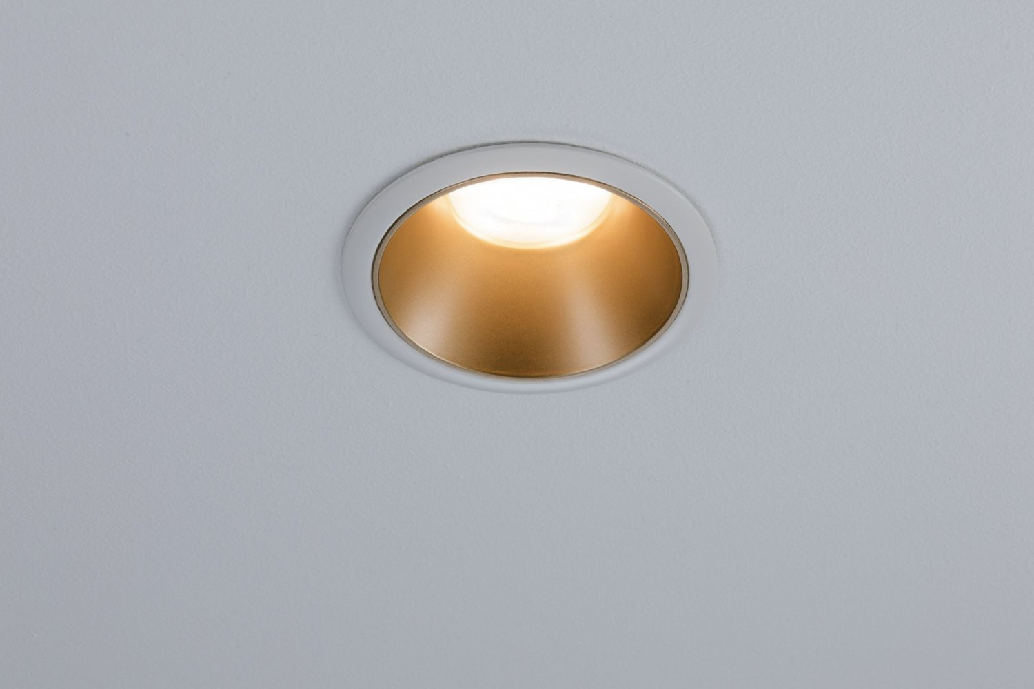 Una luce a incasso a soffitto con un interno dorato e un anello esterno bianco.