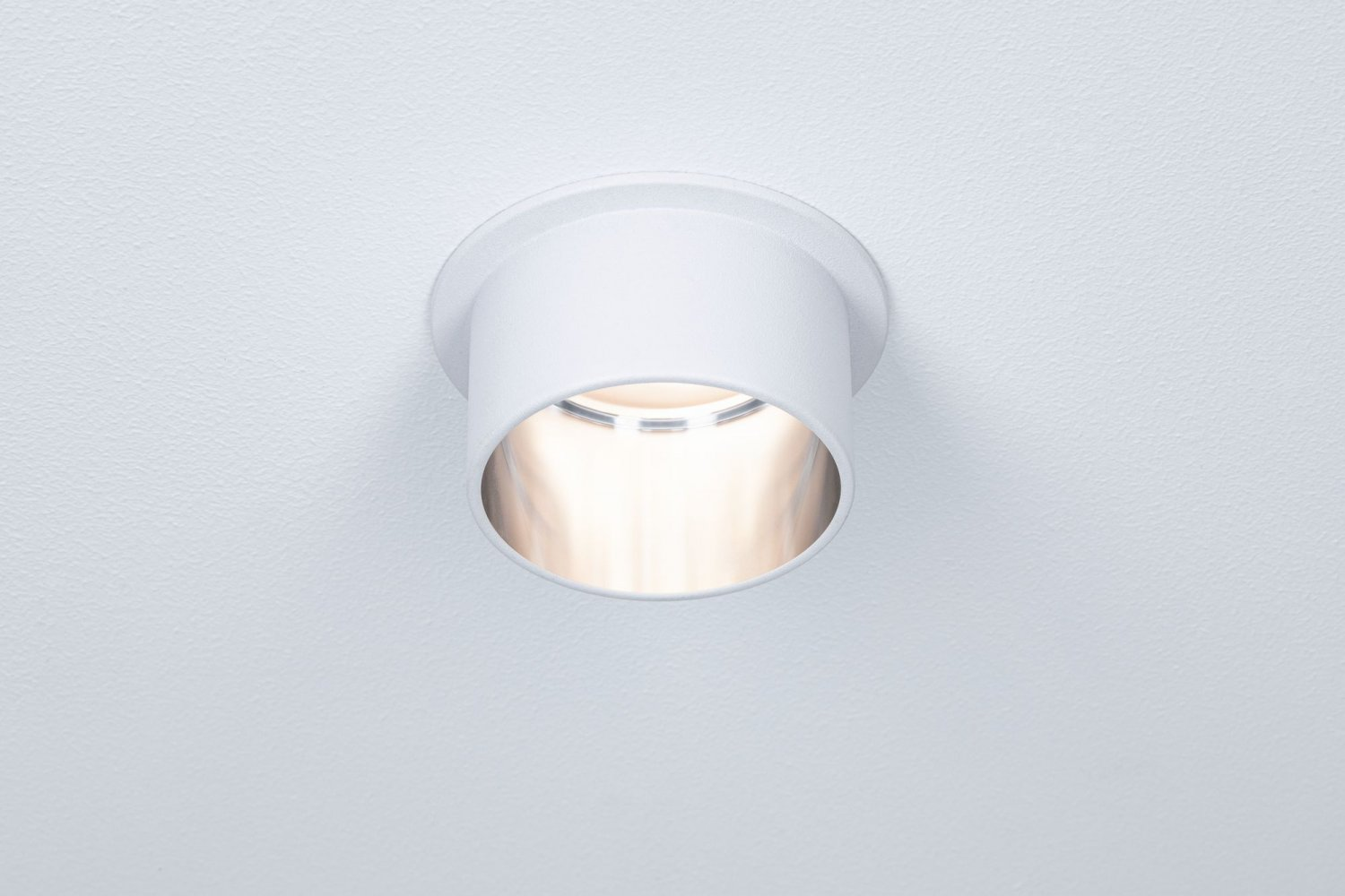 Weiße Einbau-Deckenleuchte, die Licht aussendet, vor weißer Decke.