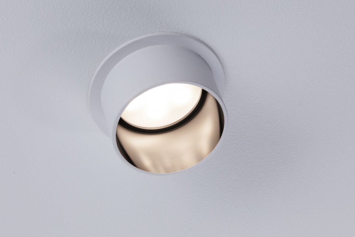 Ein weißer Einbaustrahler in einer weißen Decke, wobei die Lichtquelle sichtbar ist.