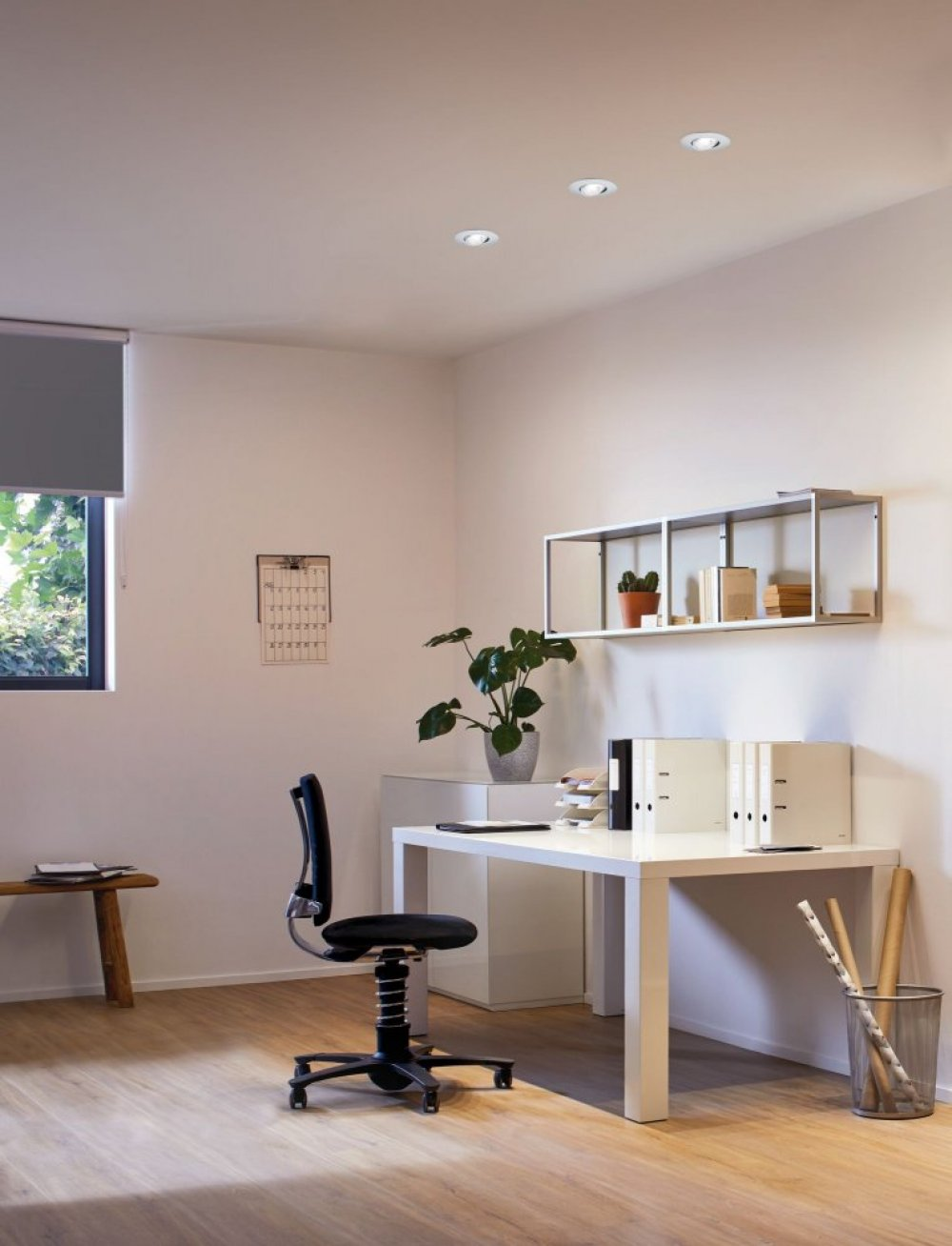 Modernes Büro mit Schreibtisch, Stuhl und weißen Wänden. Drei Einbauleuchten an der Decke.