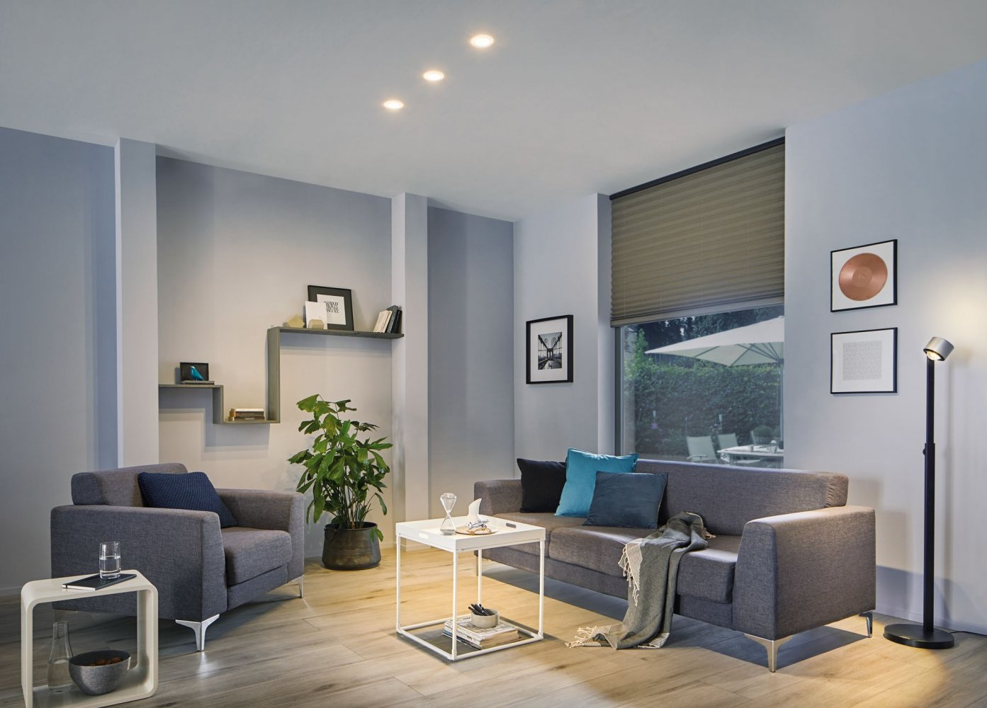 Ein Wohnzimmer mit grauem Sofa, Sesseln und einem weißen Couchtisch. Natürliches Licht vom Fenster.