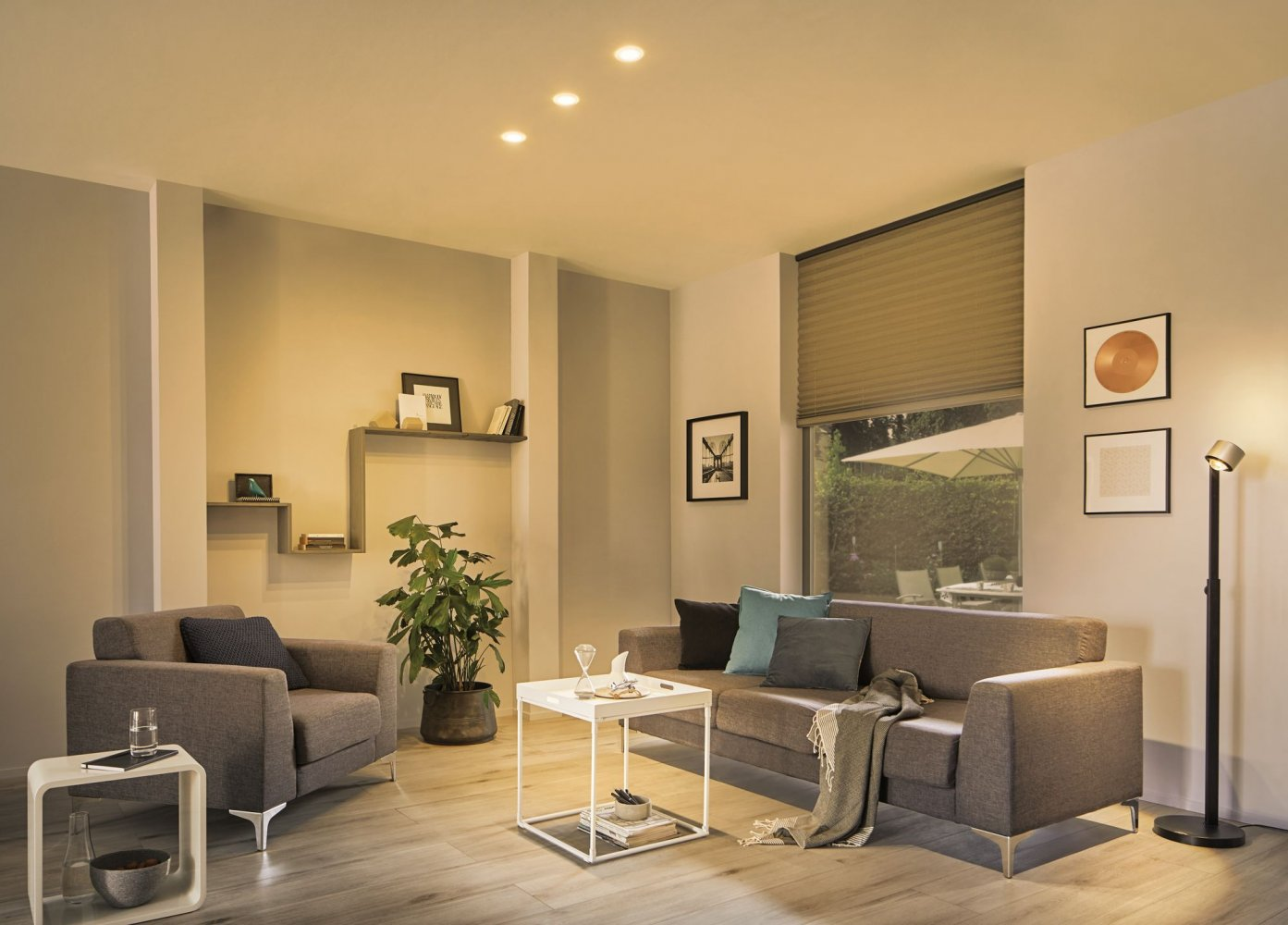 Wohnzimmer mit Sofa, Sesseln und Einbauleuchten. Warme Beleuchtung, weiße Wände.