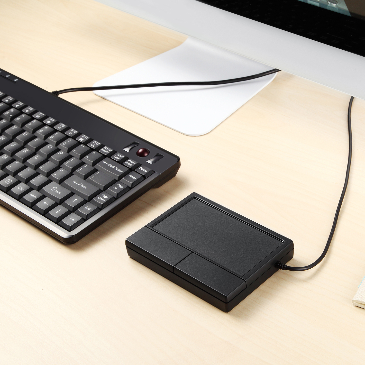 Schwarze Tastatur, schwarzes Trackpad und ein Computermonitor auf einem hellen Holztisch.