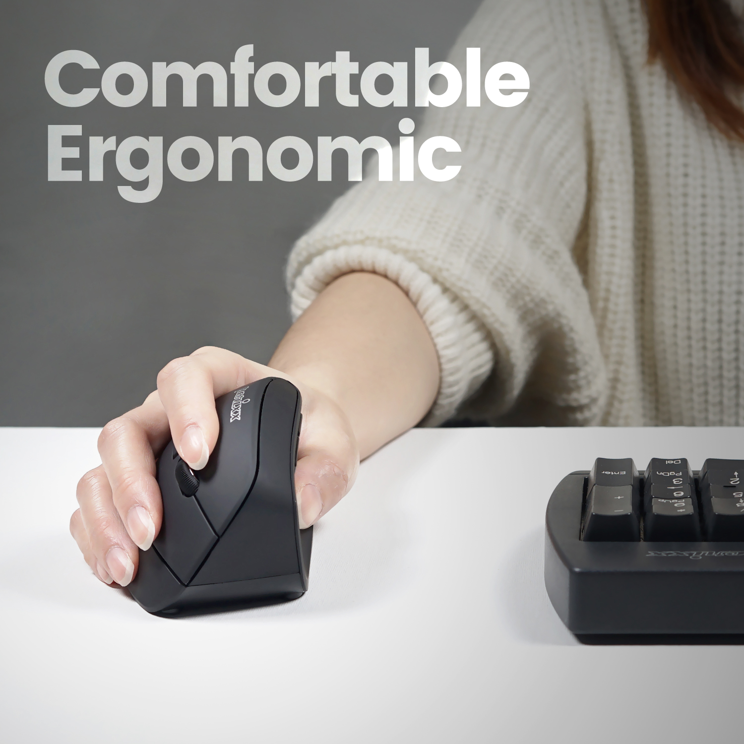 Die Hand einer Person, die eine schwarze ergonomische Maus auf einem weißen Schreibtisch neben einer Tastatur hält.
