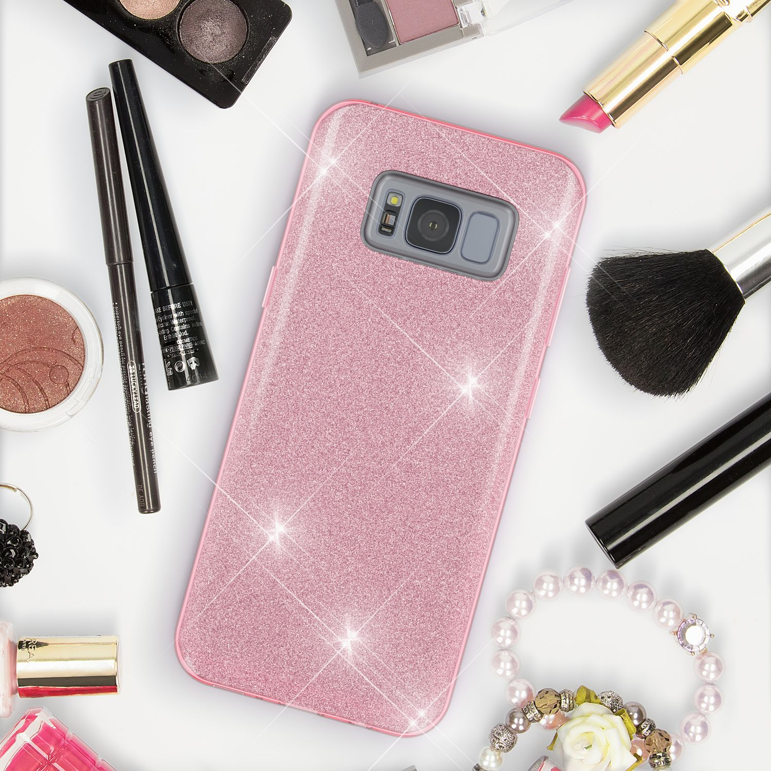 Rosa Glitzer-Handyhülle umgeben von Make-up und Accessoires. Weißer Hintergrund.