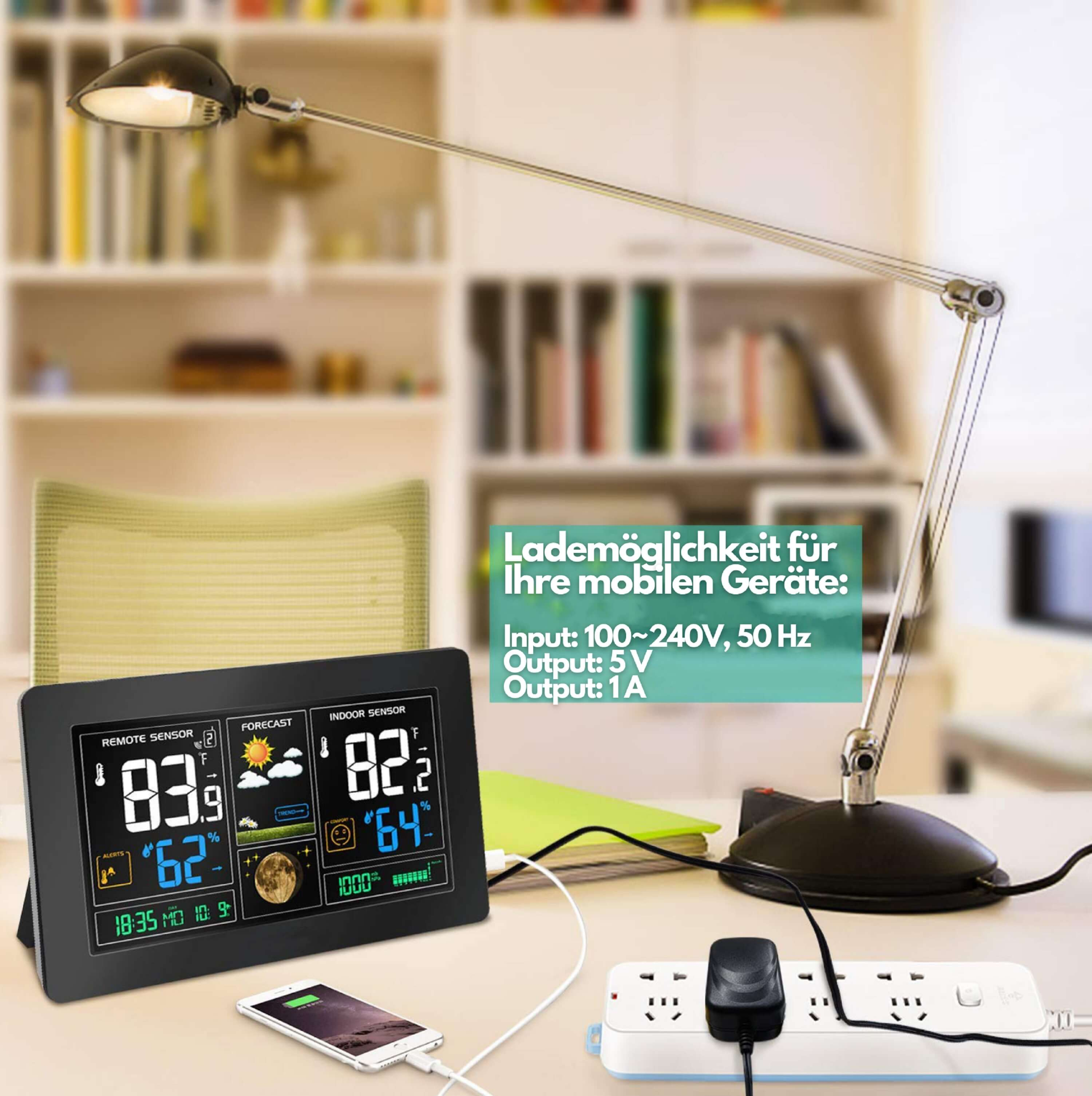 Ein Schreibtisch mit Lampe, Wetterstation, Telefonladung und Steckdosenleiste. Das Licht ist an.