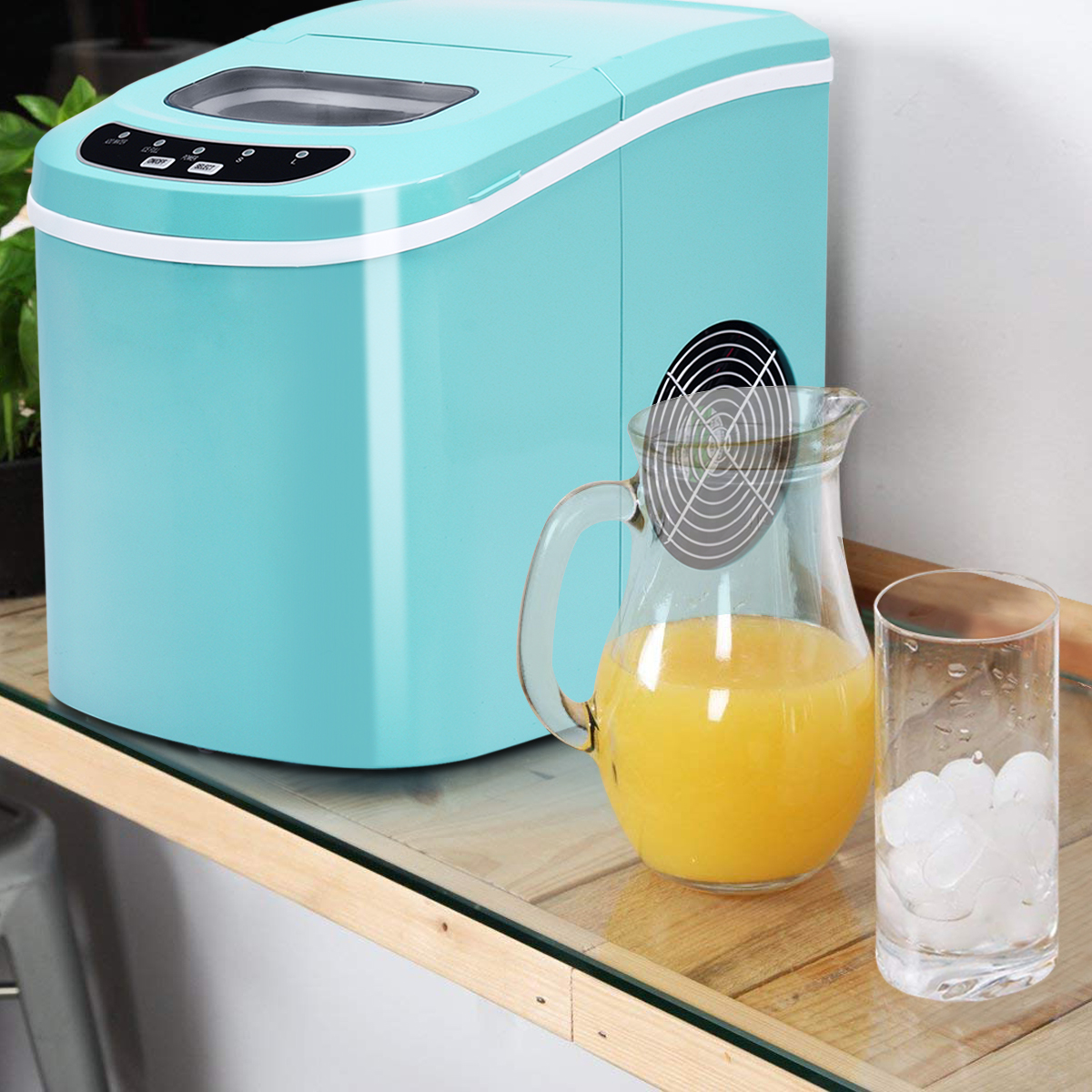 Türkisblaue Eismaschine neben einem Krug mit Orangensaft und einem Glas Eiswürfeln.