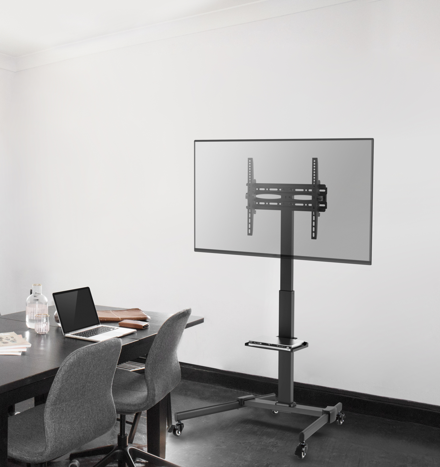 Ein Raum mit TV-Ständer, Schreibtisch mit Laptop, Flasche und zwei grauen Stühlen.
