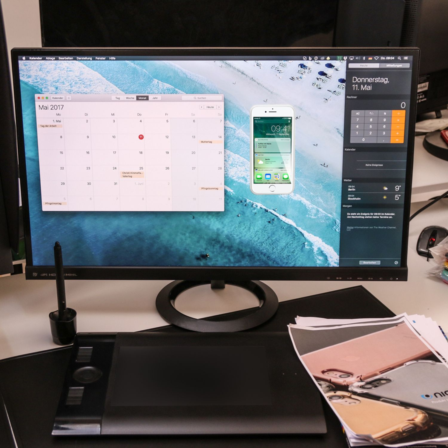 Ein Monitor mit Kalender und Telefon mit geöffneter Kalender-App. Auf dem Schreibtisch liegen weitere Dinge.