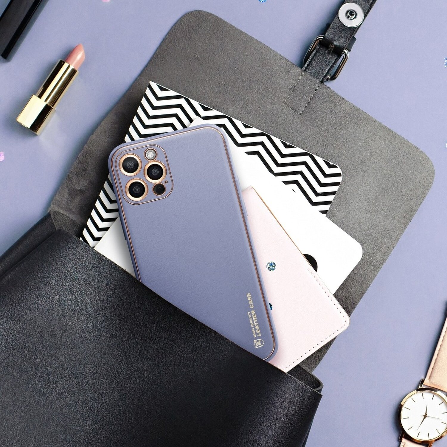 Eine Handyhülle, ein Notizbuch und Lippenstift in einer Handtasche. Der Hintergrund ist eine lila Oberfläche.