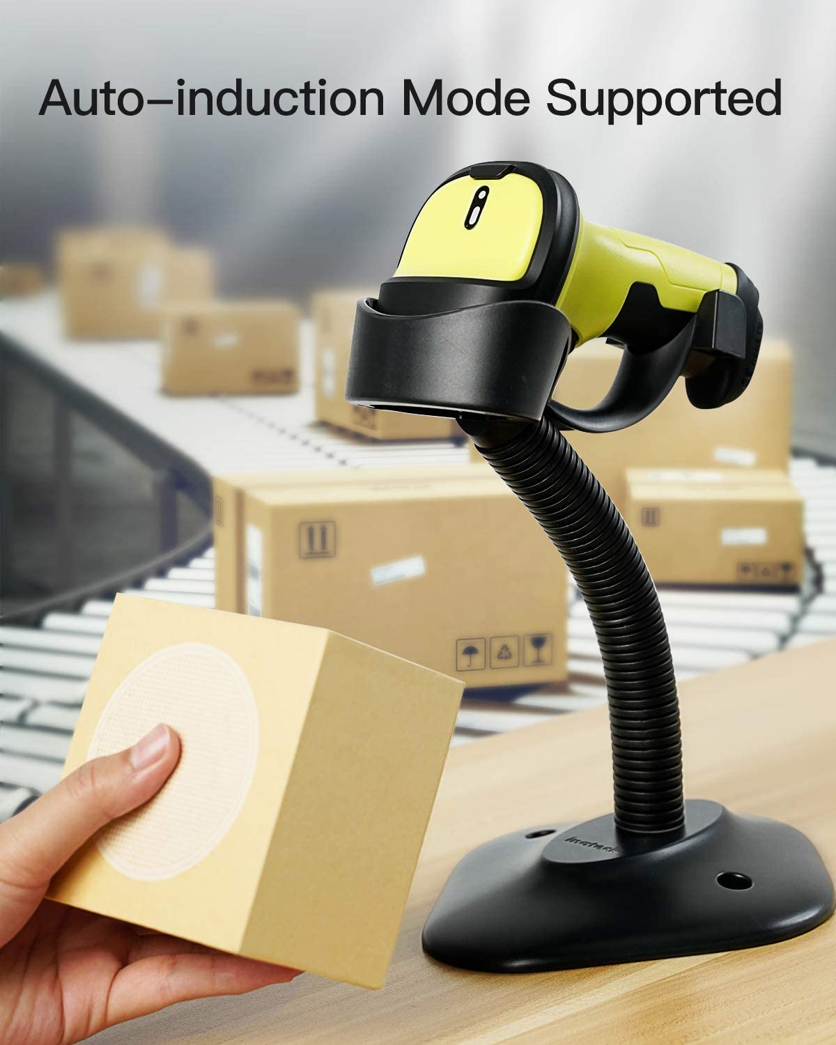 Eine Hand hält eine Box neben einem Barcode-Scanner auf einem Schreibtisch mit Boxen im Hintergrund.