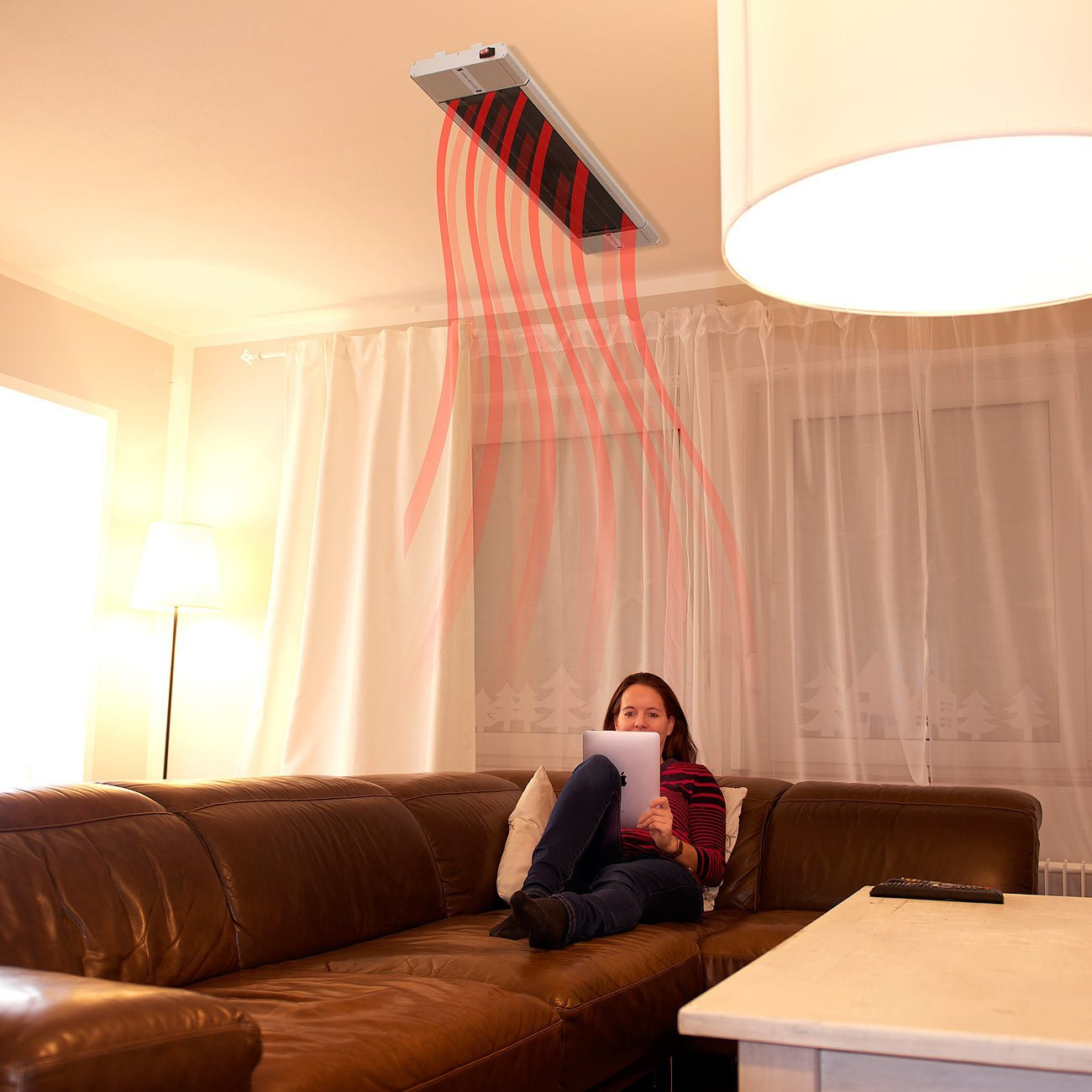 Frau auf einem braunen Sofa, die ein Tablet benutzt, ein Deckenheizstrahler ist an.