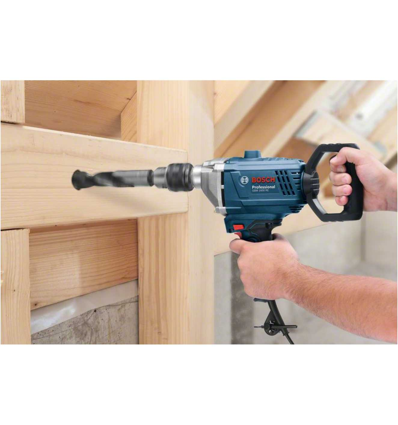 Wiertarka Bosch wierci w drewnie. Jedna ręka trzyma wiertarkę, druga trzyma drewno.