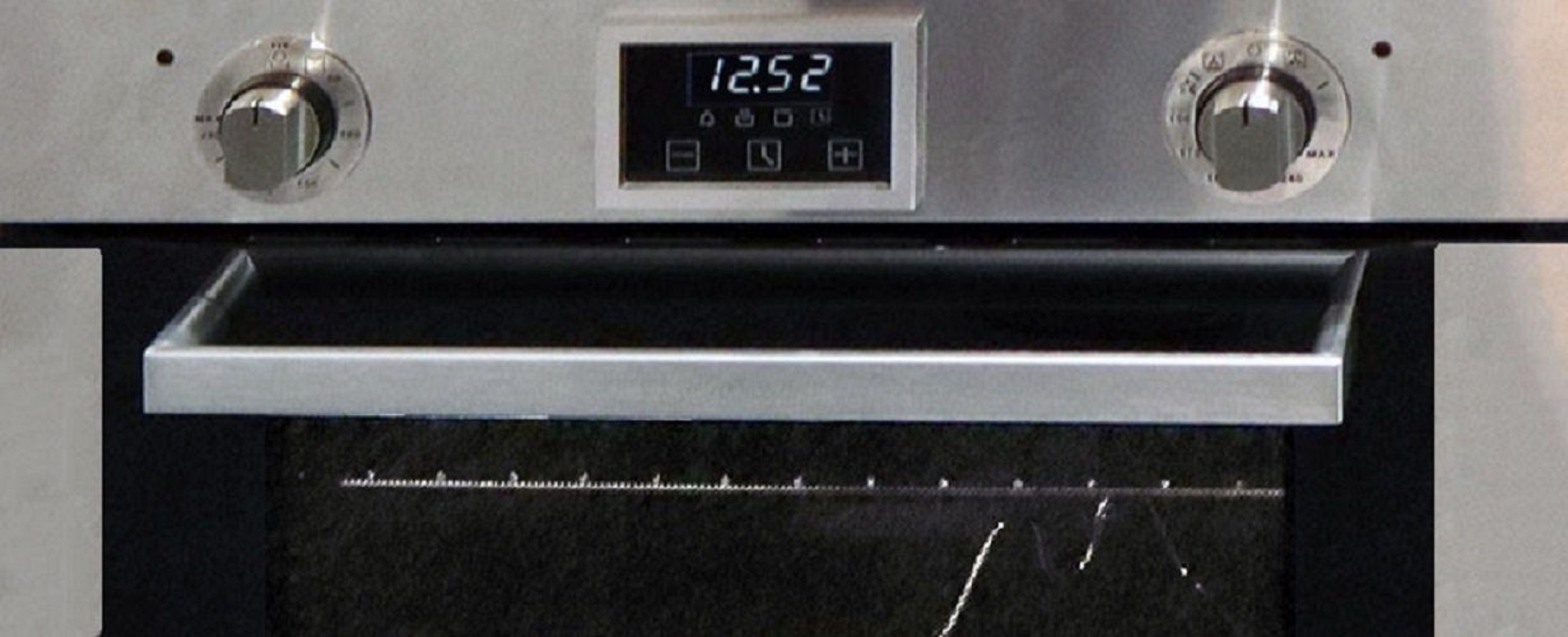 Nahaufnahme eines Ofens mit digitaler Uhranzeige, zwei Bedienknöpfen und einem Griff.