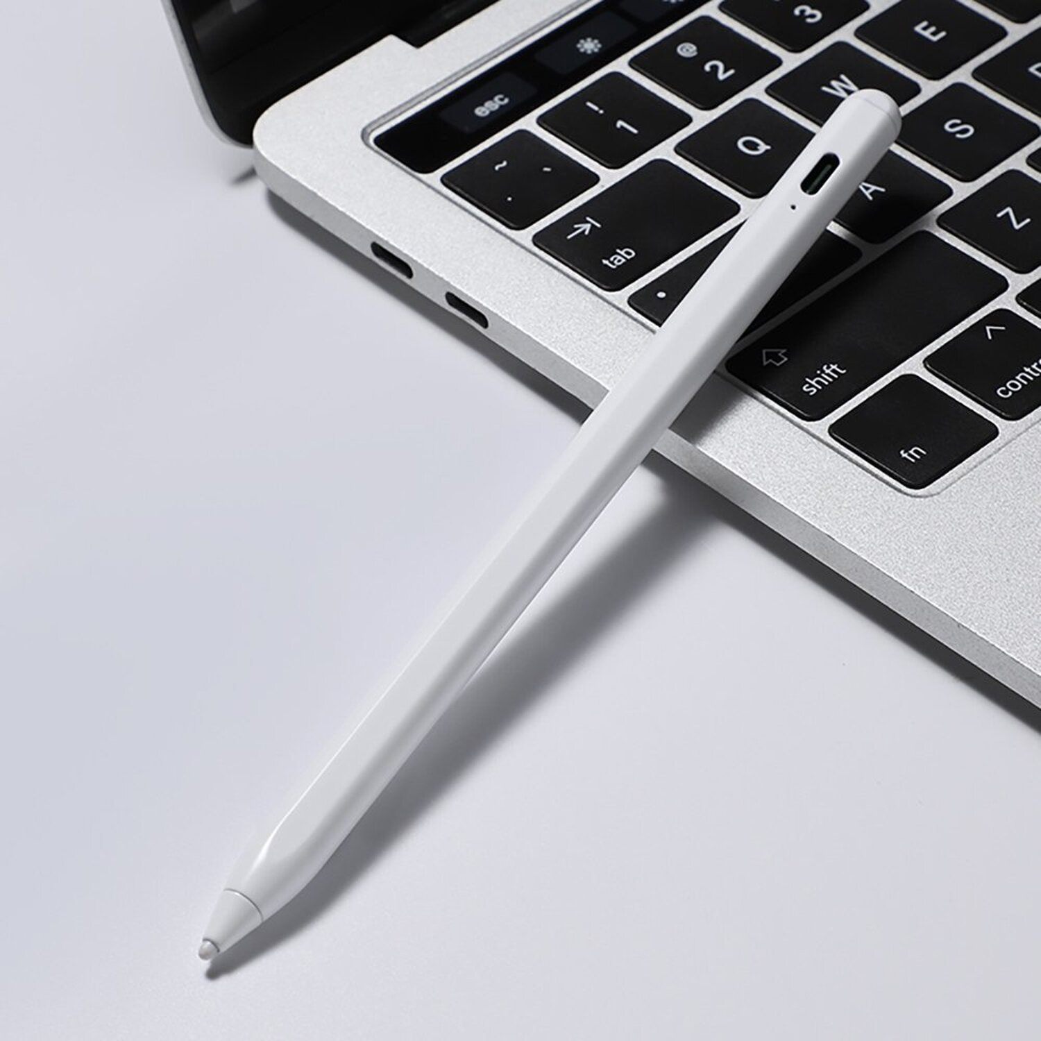 Ein weißer Stift liegt auf einer Laptop-Tastatur. Die Tastatur ist silberfarben.